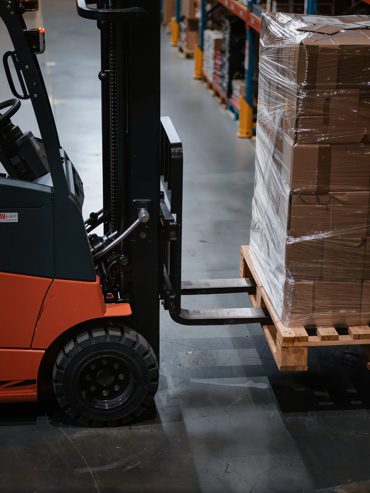 Forklift forks lining up with the pockets of a pallet stacked with wrapped boxes