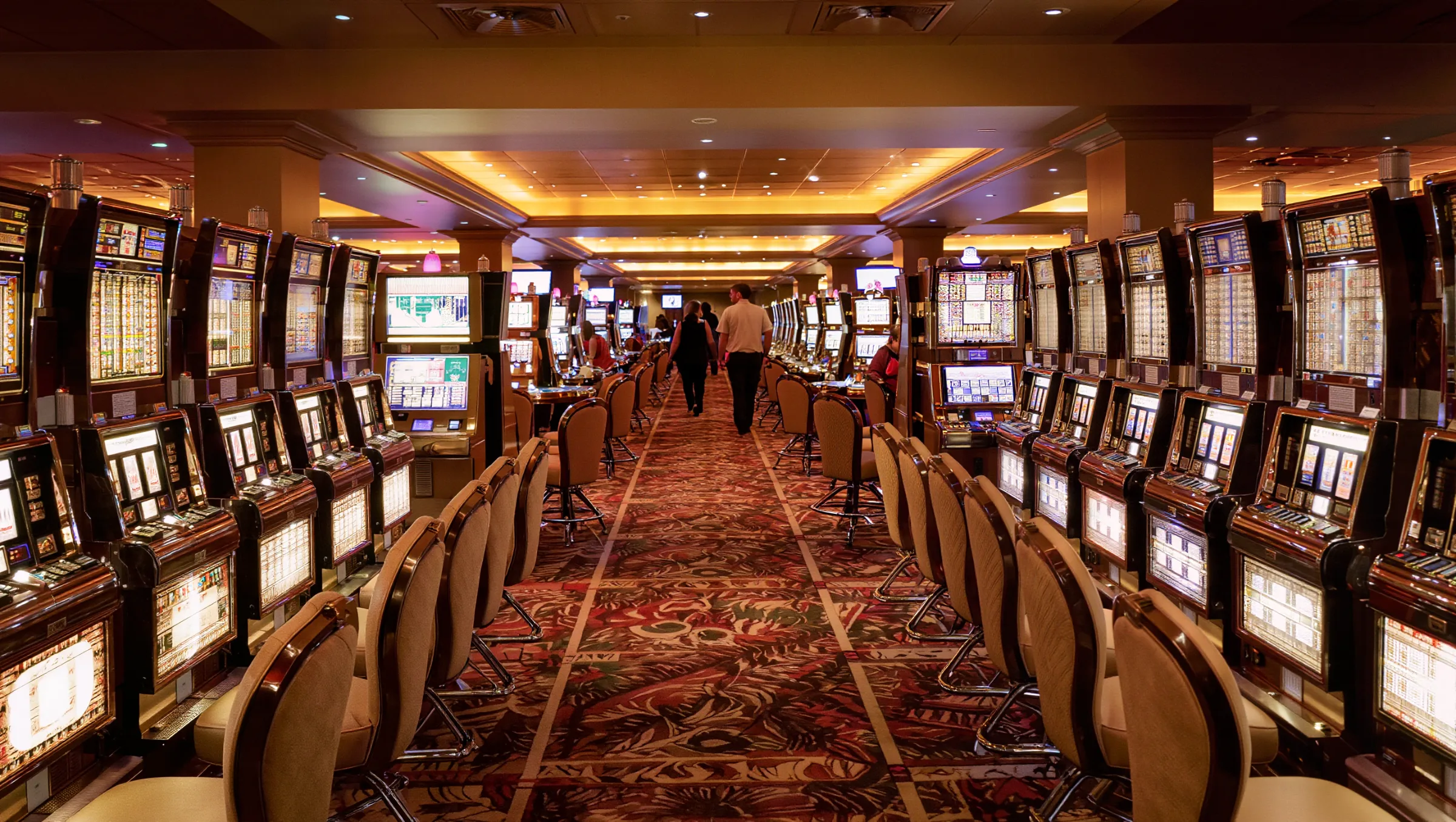 Casino gaming floor with a long aisle of slot machines and a few guests