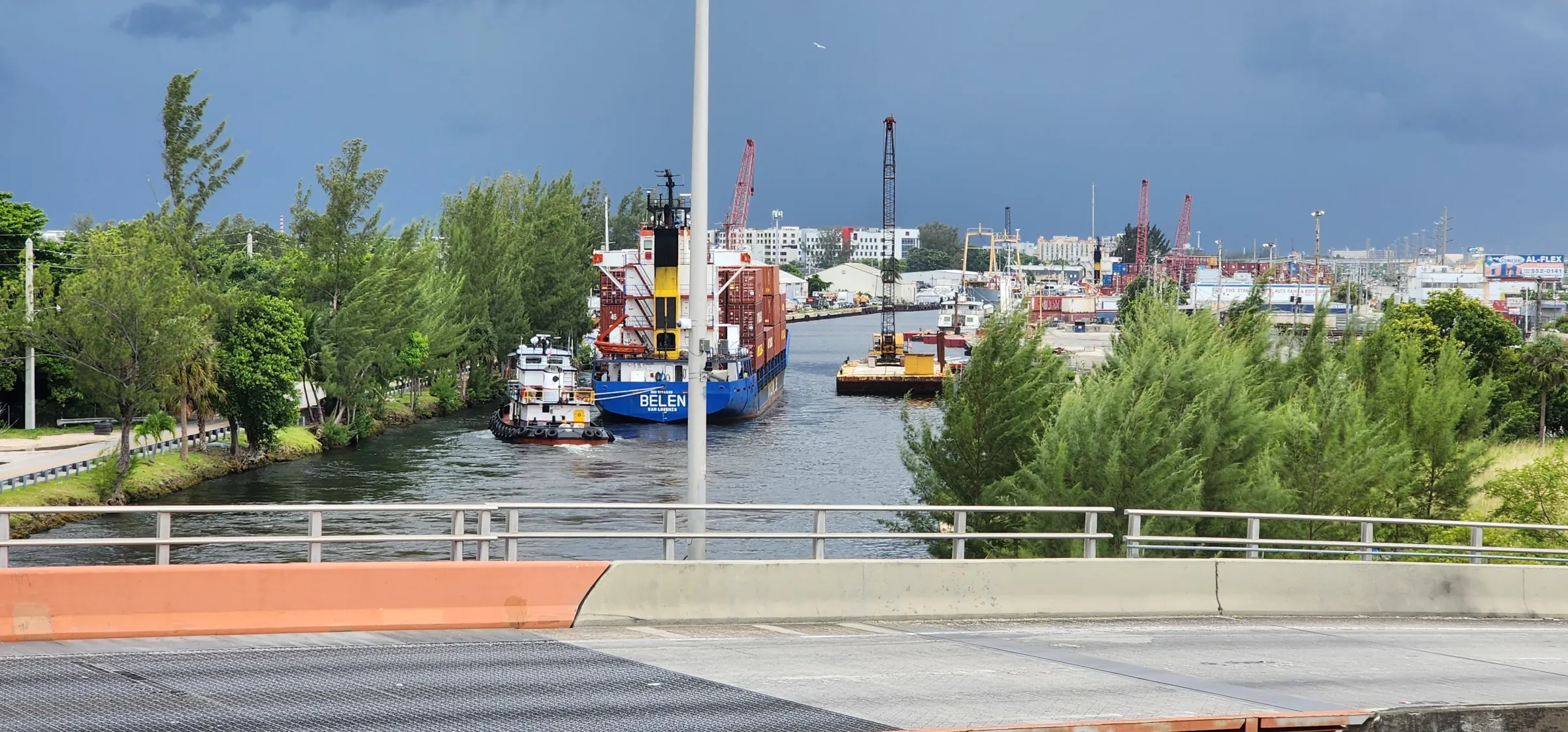 Cargo ship and tugboat passing a movable bridge on a river, seen from the bridge deck