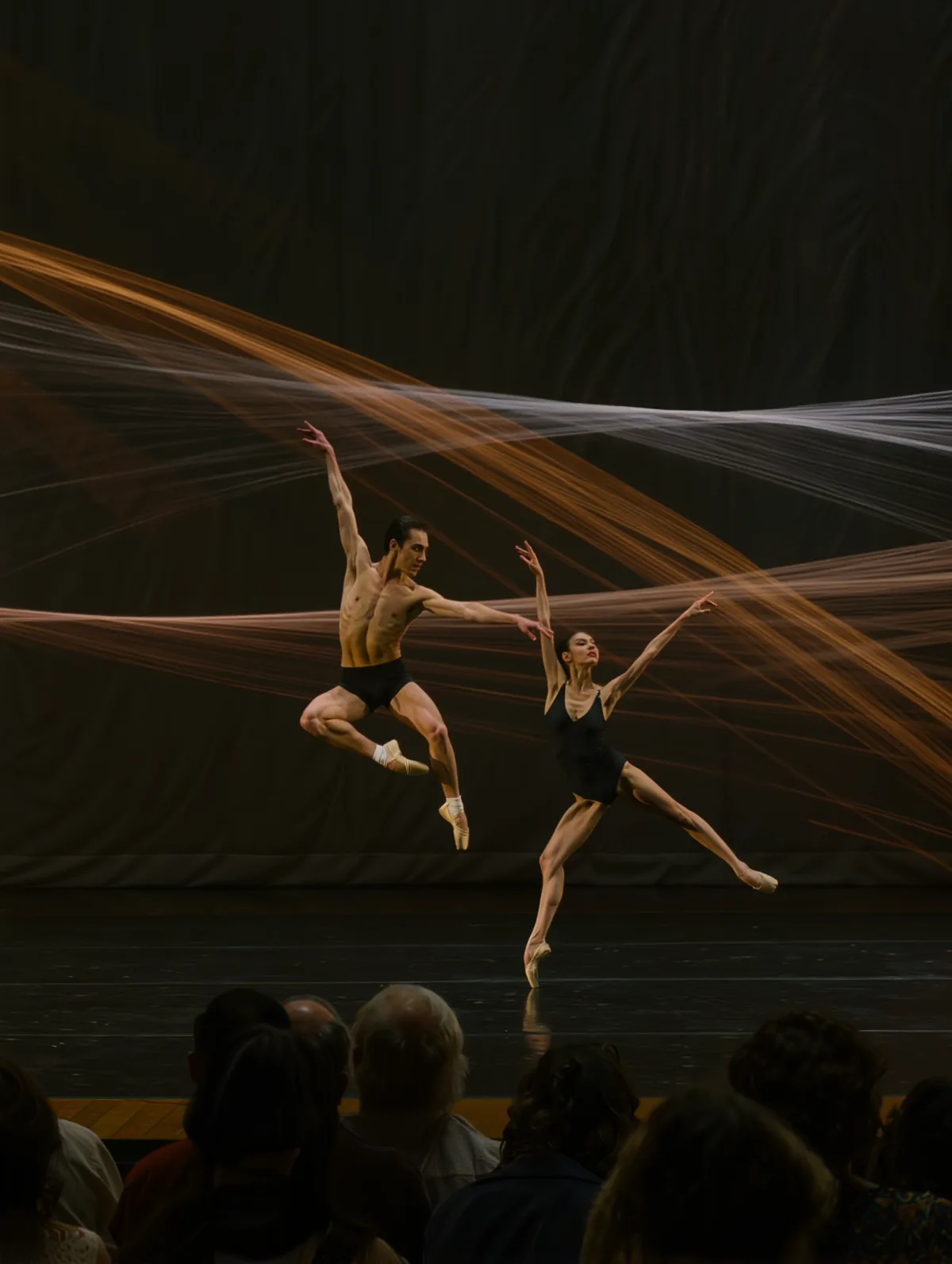 Dancers on a dark stage with projected light trails following their movement