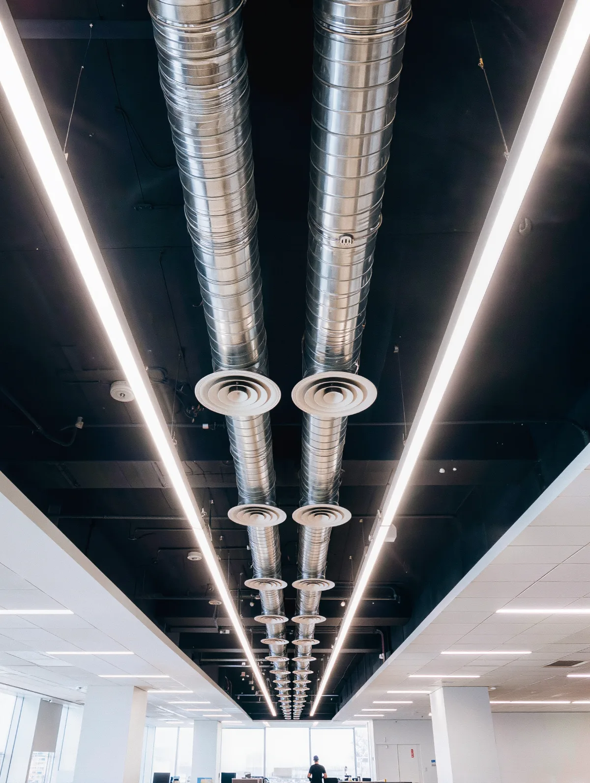 Exposed HVAC ductwork and air diffusers above a bright open-plan office